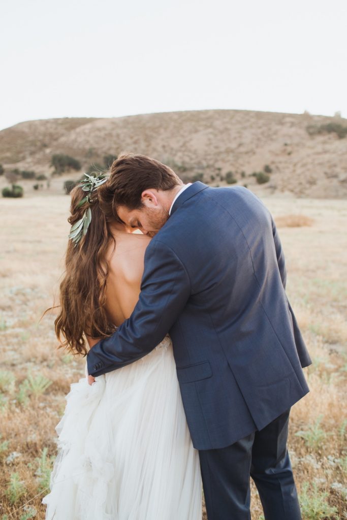 groom kissing bride's shoulder in a field