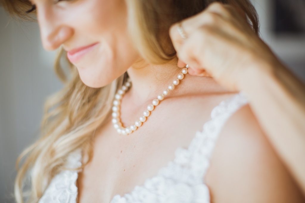 bride putting on pearl necklace